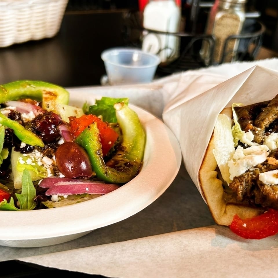 A gyro with meat and feta cheese next to a fresh salad with bell peppers and red onions.