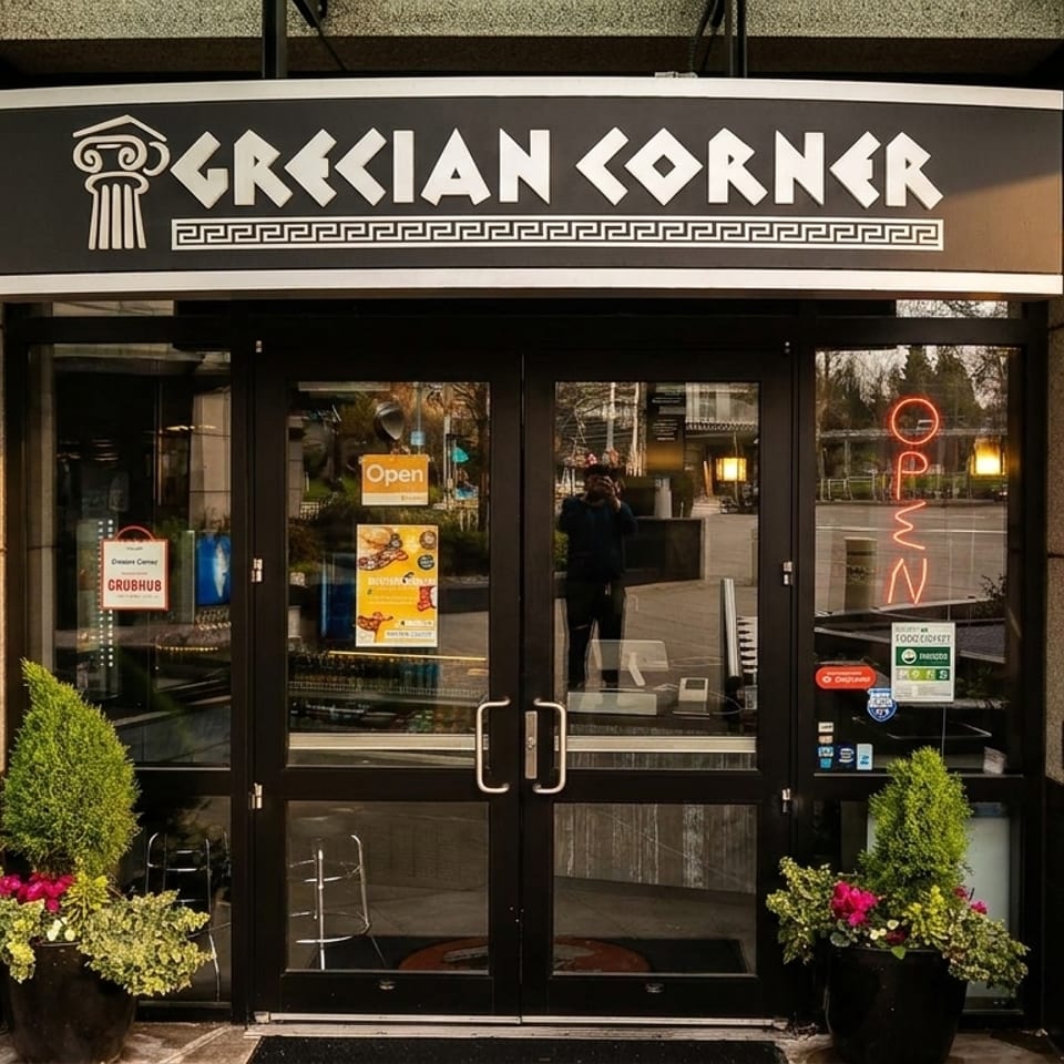 Exterior of "Grecian Corner" restaurant with a black sign, glass doors, and potted plants.
